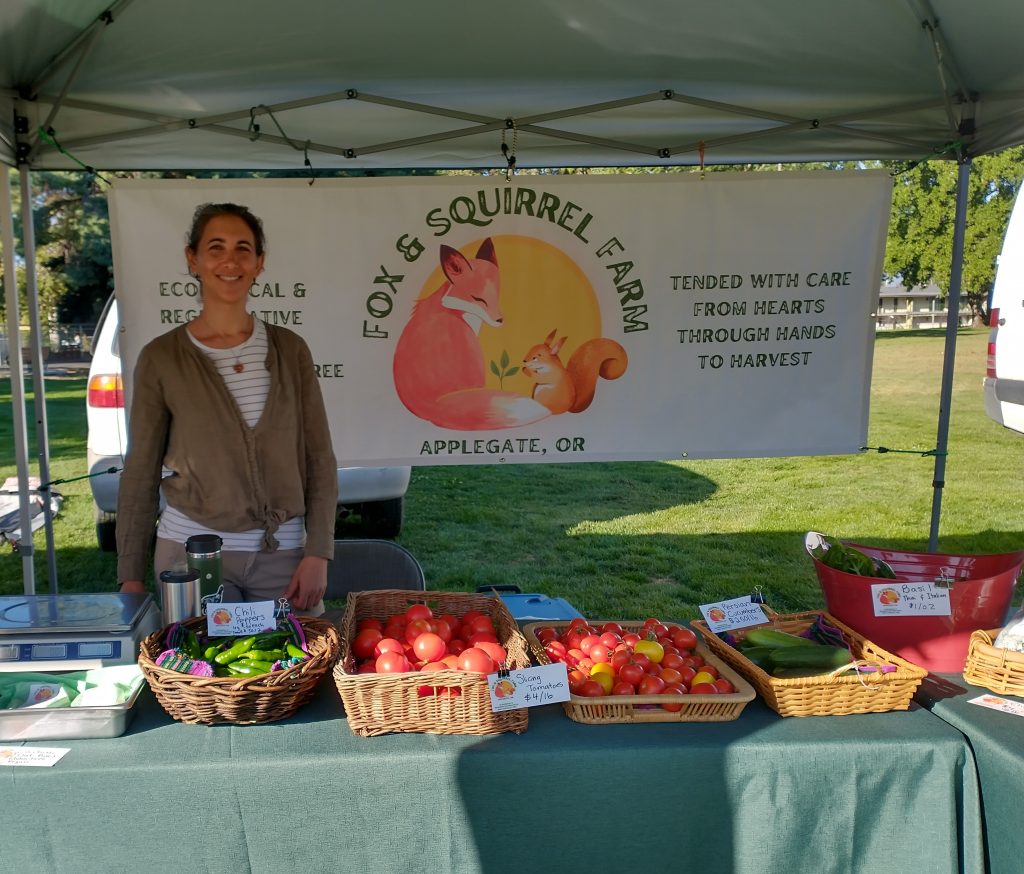 Jennifer from Fox and Squirrel Farm presenting a selection of organic produce at a local market stand